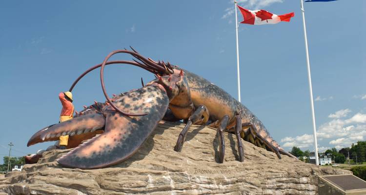 Une gigantesque statue de homard avec des drapeaux canadiens se dresse contre un ciel bleu dégagé.
