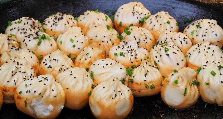 Des raviolis à soupe fraîchement poêlés saupoudrés de ciboulette et de graines de sésame grésillent dans une grande poêle.