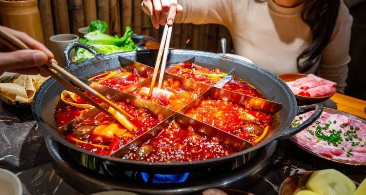Les convives partagent un hot pot de Chongqing fumant à neuf compartiments débordant de bouillon rouge épicé, de viandes et de légumes.