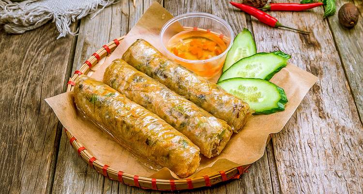 Three freshly prepared fried spring rolls with dipping sauce.