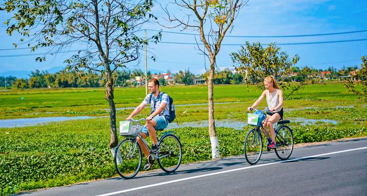 Cyclists riding along a rural road with farmland in the background.