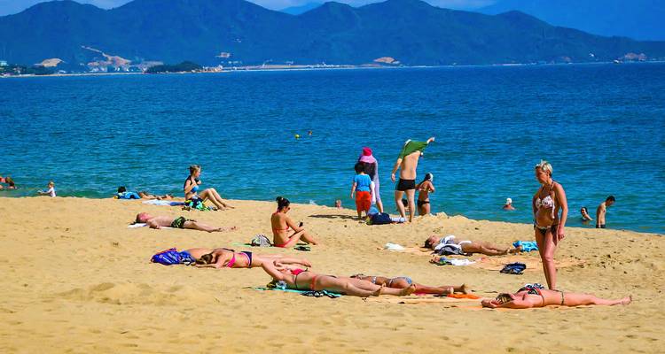 Menschen, die sich sonnen und einen Sandstrand mit fernen Bergen genießen.