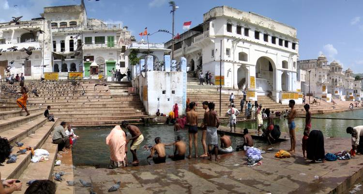 Personas bañándose en un tanque de agua público rodeado de edificios tradicionales.