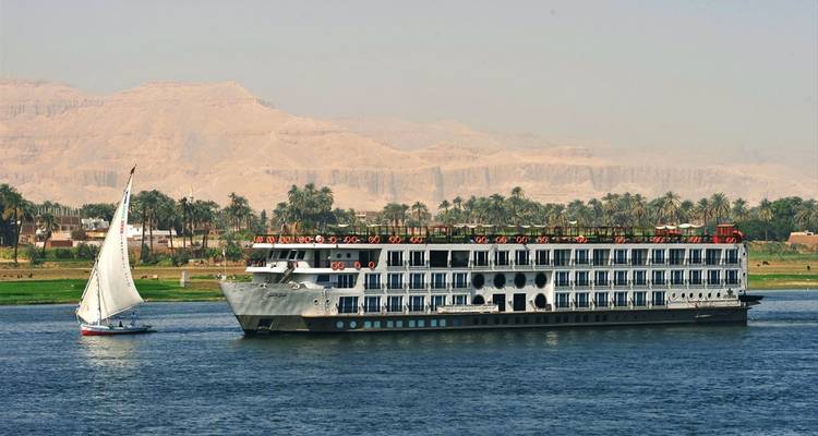 Ein Kreuzfahrtschiff und ein Segelboot auf dem Nil mit Wüstenlandschaft.