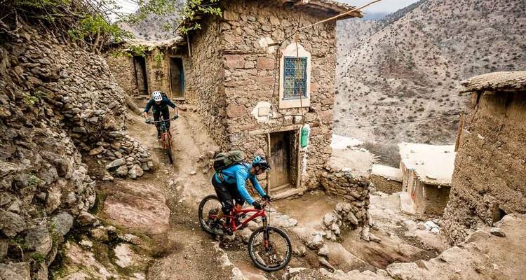 Zwei Mountainbiker fahren durch einen schmalen Dorfweg.