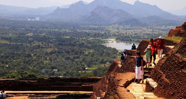 Personas caminando sobre ruinas antiguas con un paisaje montañoso al fondo.