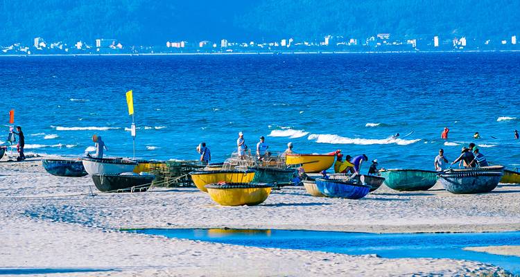 Personas disfrutando de una playa con botes redondos tradicionales en primer plano.