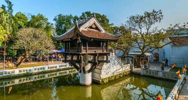 Tempel op palen boven een vijver omringd door bomen.