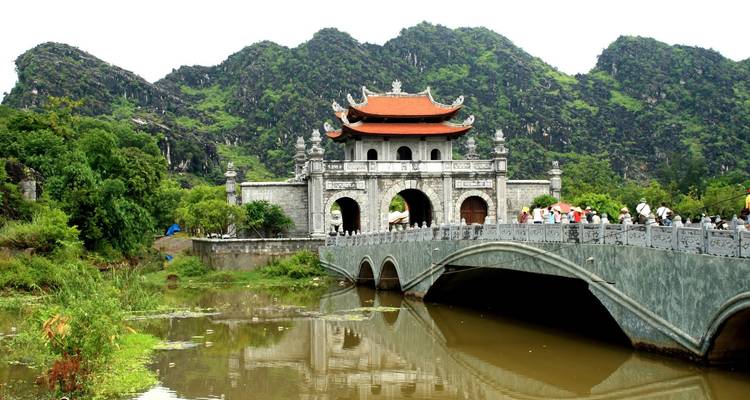 Ancient gatehouse with a bridge and green hills in the background.