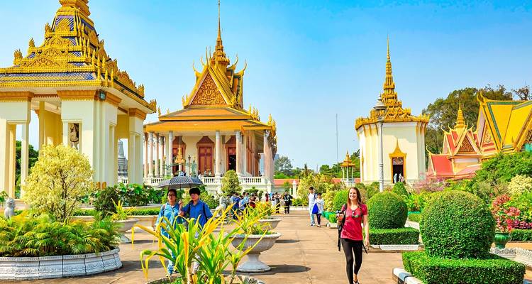 Visitors in a well-maintained garden with traditional buildings featuring golden roofs.