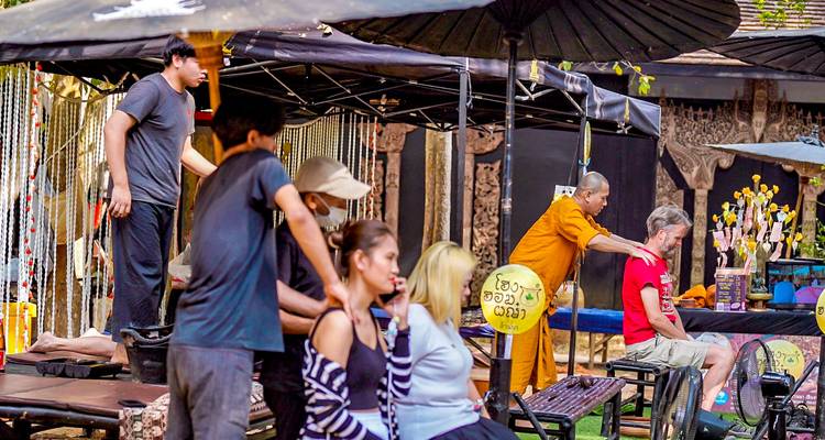 Groupe de personnes recevant des massages dans un cadre extérieur avec un moine offrant un massage.