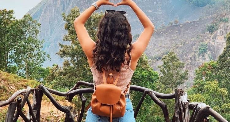 Vista posterior de una mujer haciendo un gesto de corazón en un valle exuberante.