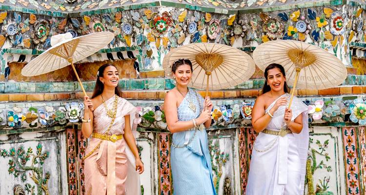 Tres mujeres en atuendo tradicional con sombrillas, frente a una pared decorada.