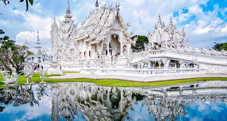 Templo blanco intrincado rodeado de reflejos en un estanque tranquilo.
