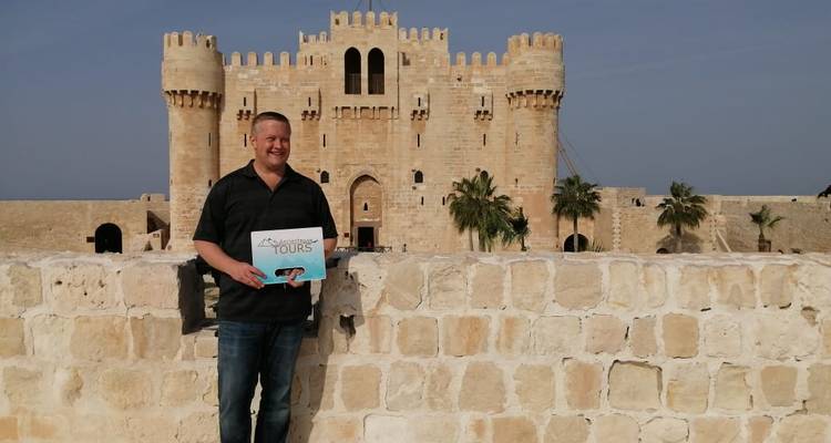 Mann, der ein Schild hält, mit einer historischen Festung im Hintergrund.