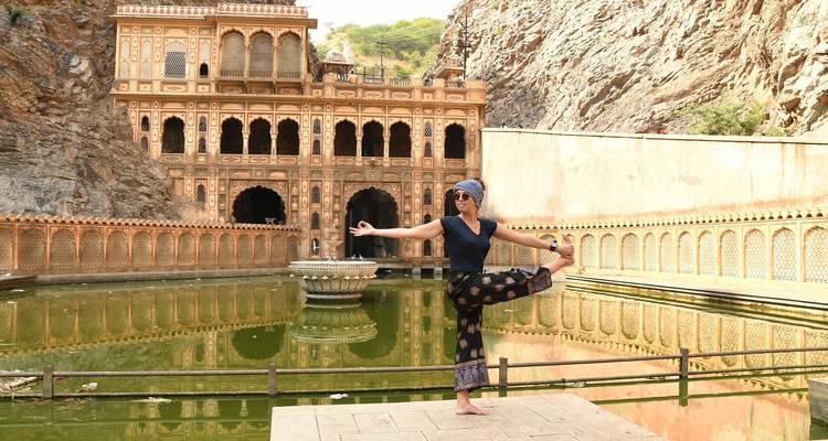 Person, die Yoga vor einem Tempel praktiziert, mit Wasser im Vordergrund.