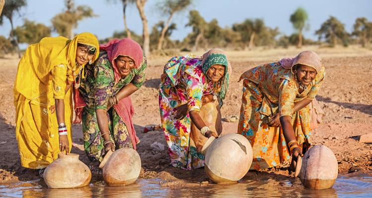 Women in colorful dresses collecting water with pots.