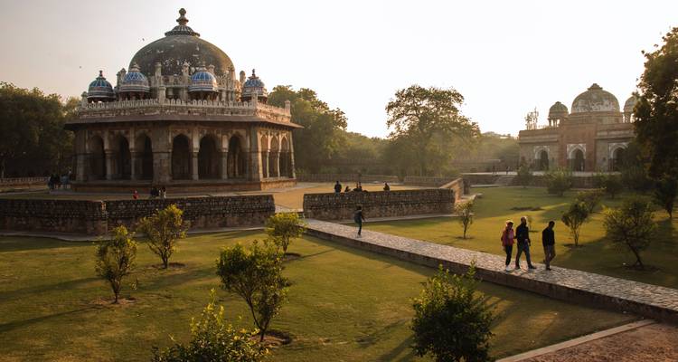 Menschen, die in einem Garten in der Nähe alter kuppelförmiger Gebäude spazieren gehen.