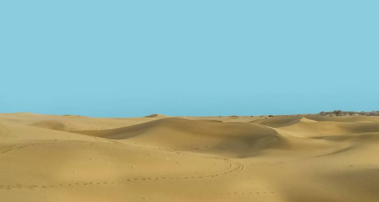 Uitgestrekt zandig woestijnlandschap onder heldere blauwe lucht.