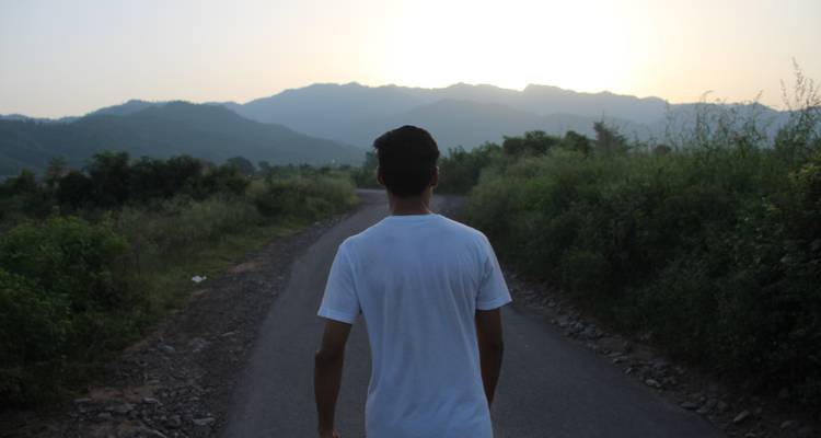 Person walking on a road surrounded by greenery and hills.