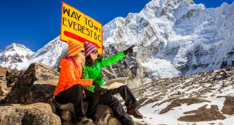 Zwei Wanderer sitzen mit einem Schild, das zum Everest-Basislager zeigt.