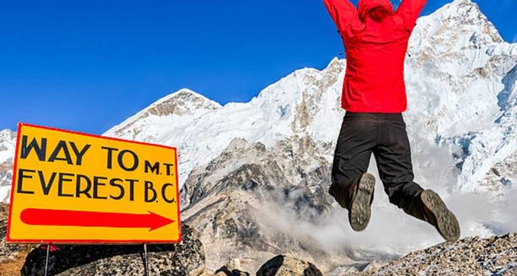 Person springt mit einem Schild, das den Weg zum Everest-Basislager anzeigt.