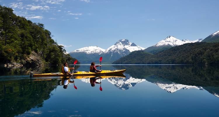 Deux kayakistes pagayant sur un lac avec des montagnes en arrière-plan.