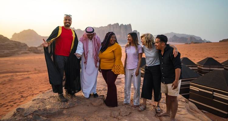 Petit groupe avec hôte bédouin pose sur le sable rouge au milieu des formations rocheuses du Wadi Rum au coucher du soleil.