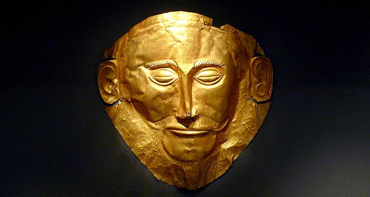 Gold funerary mask with detailed facial features displayed in a museum setting.