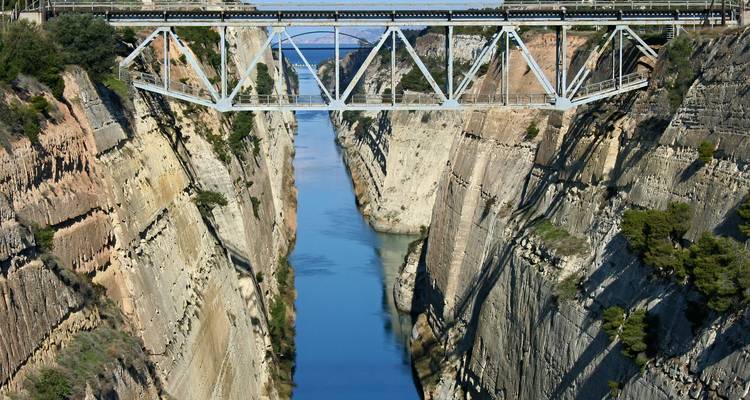 Canal estrecho bajo un puente de acero con un tren pasando por encima.