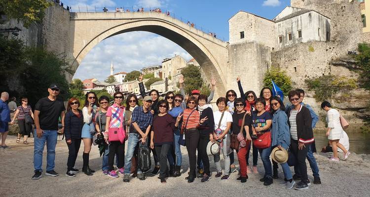 Touristen posieren vor einer historischen Brücke und einem Fluss.