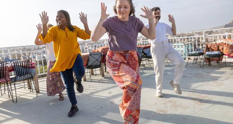 Groep toeristen die energiek dansen op een zonnig dakterras met uitzicht over een Indische stad.