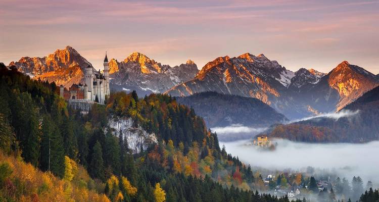 Un château célèbre se dressant contre des montagnes brumeuses et une forêt d'automne éclatante.