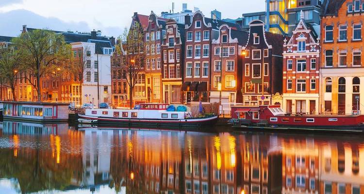 Les maisons de canal historiques d'Amsterdam et les bateaux se reflétant dans les eaux calmes du crépuscule.