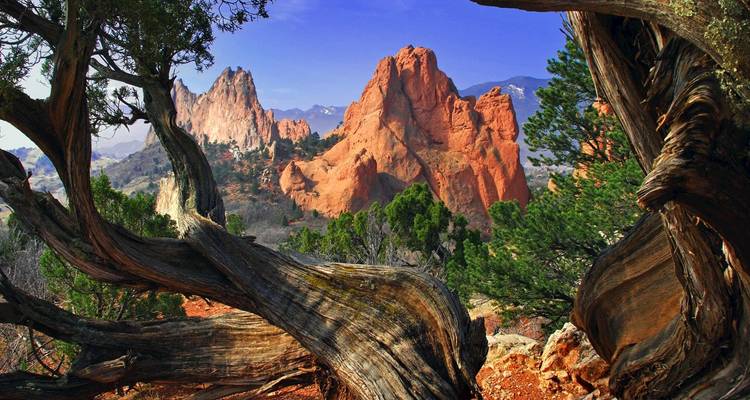Dramatische rotsformaties omringd door bomen en blauwe luchten.