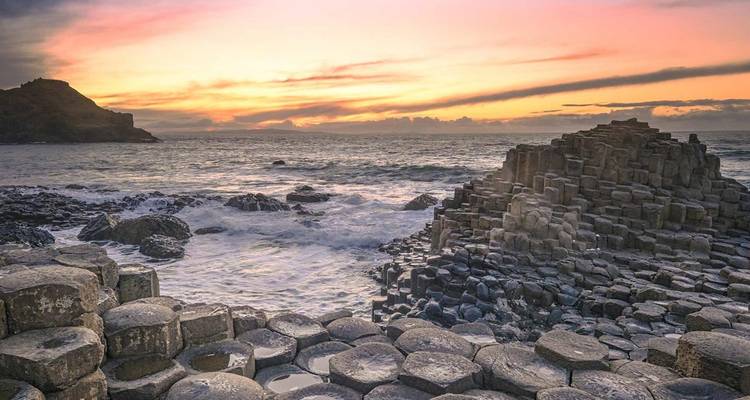 Les colonnes de basalte de la Chaussée des Géants rencontrent les vagues qui se brisent au coucher du soleil avec un ciel coloré.