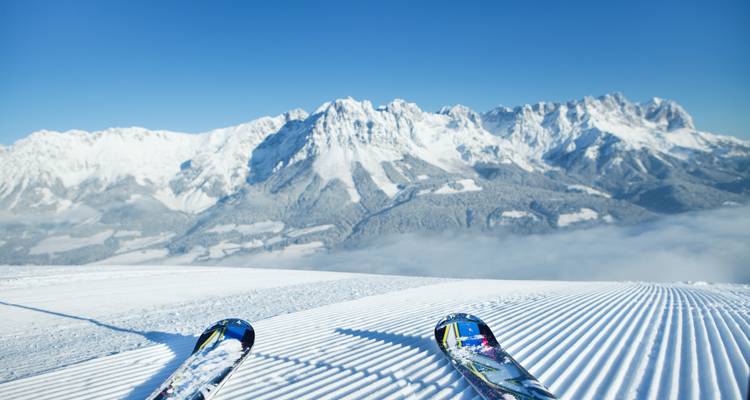 Une paire de skis repose sur une piste fraîchement préparée surplombant une chaîne de montagnes spectaculaire couverte de neige.