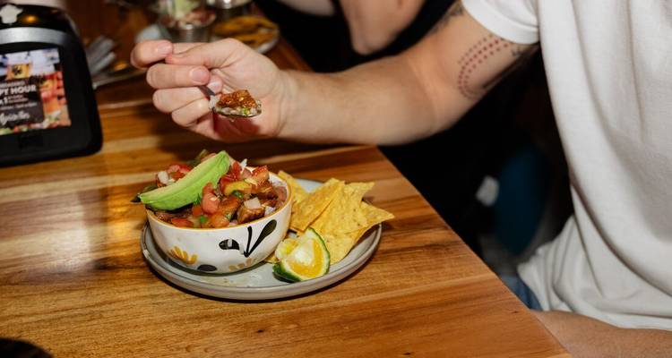 Persoon die guacamole en chips eet in een restaurant.