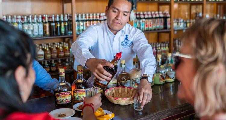 Barkeeper, der Mezcal-Kostproben für Besucher in einer rustikalen Bar mit Spirituosenflaschen ausschenkt