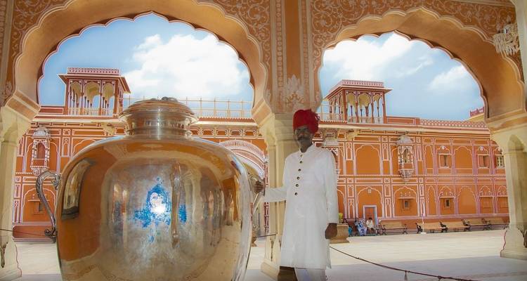 Une personne vêtue traditionnellement se tenant à côté d'un grand récipient argenté à l'intérieur d'une architecture ornée.