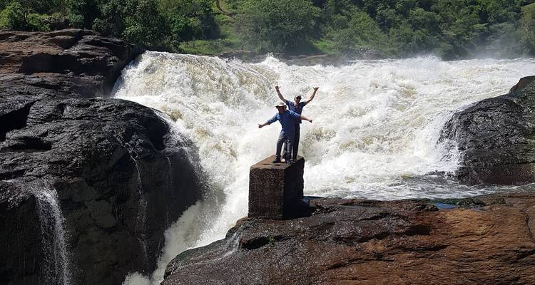 Personas paradas en una roca cerca de las cataratas, levantando las manos con emoción.