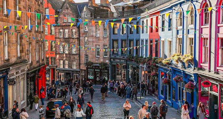 Escaparates coloridos y banderines adornan la animada calle empedrada Victoria Street en Edimburgo llena de peatones.