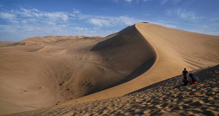 Personas caminando en una duna de arena bajo un cielo azul.