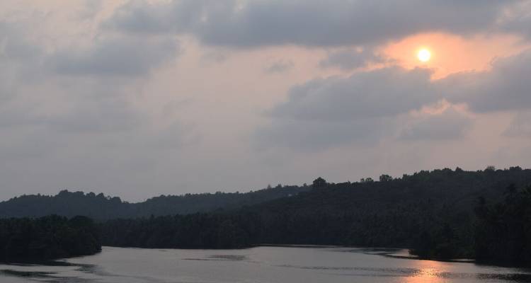 Coucher de soleil doux sur une rivière sinueuse flanquée de collines boisées sous des nuages brumeux