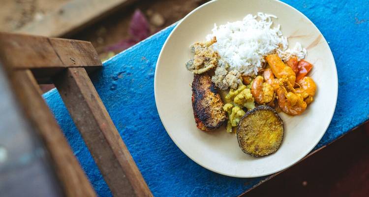 Assiette colorée de curry, riz et poisson grillé sur une table bleue rustique