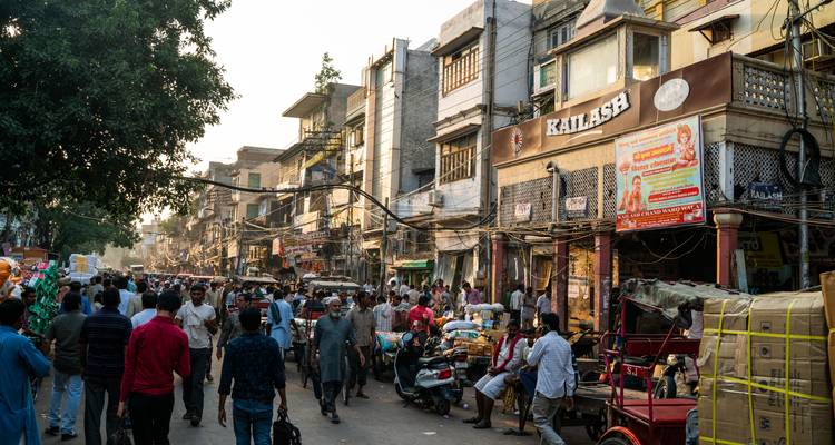 Une rue de marché animée du Vieux Delhi est remplie de piétons, de rickshaws et de devantures de magasins dans une lumière chaude du soir.