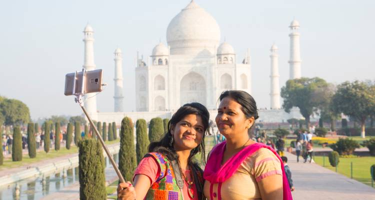 Deux femmes prennent un selfie avec l'emblématique Taj Mahal en marbre blanc qui s'élève majestueusement derrière elles.