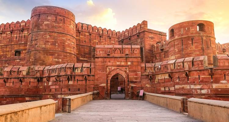 Les imposants murs de grès rouge et la porte du Fort d'Agra brillent sous un ciel pastel du soir.