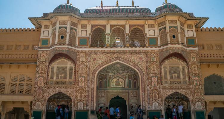 Des visiteurs se tiennent sous la porte Ganesh Pol aux peintures complexes du Fort d'Amber sous un ciel dégagé.