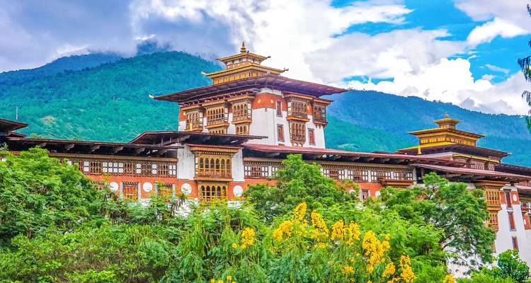 Ein großes traditionelles bhutanesisches Gebäude mit Bergen und Grün im Hintergrund.